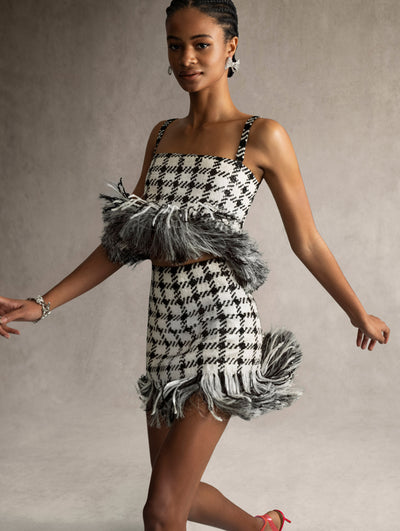 The model is wearing a matching mini skirt and crop top with a black and white checkered pattern and fringe detailing. 