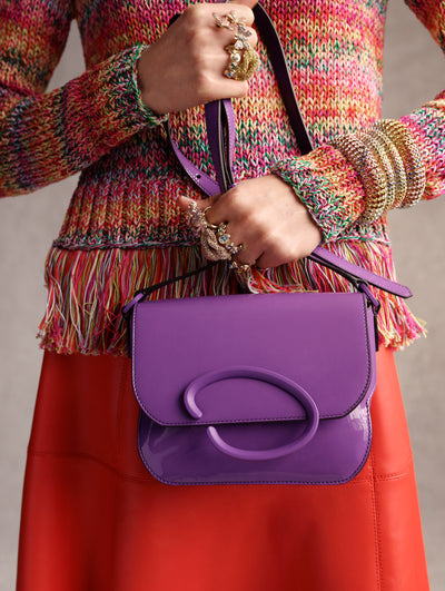 The model is carrying the purple O handbag and wearing a rainbow crochet sweater and orange leather skirt. 