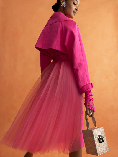 The model is wearing a pink tulle trench coat and carrying a sequin handbag. 