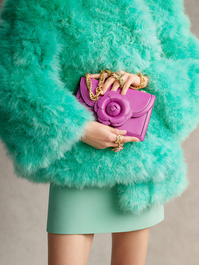 The model is carrying a pink handbag with a flower at the clasp and a teal fur jacket. 