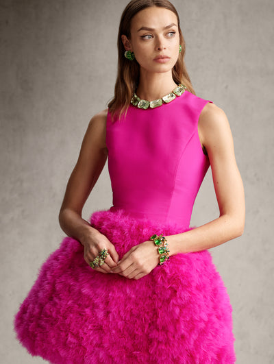 The model is wearing a pink mini dress with a high neck and ruffled skirt. 