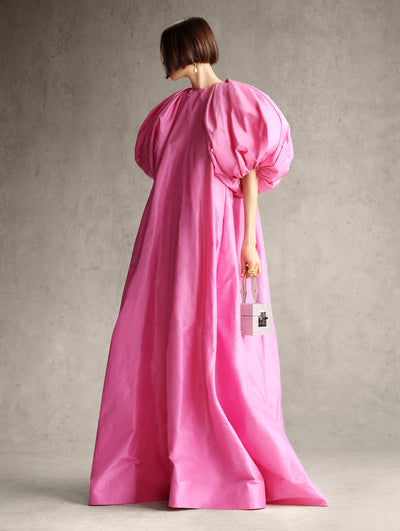 The model is wearing a large pink gown with exaggerated sleeves. 