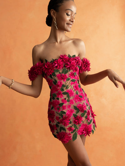 The model is wearing an off-the-shoulder pink mini dress with bright pink floral applique. 