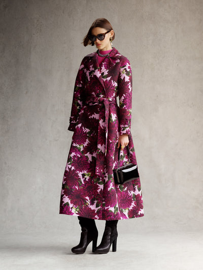 The model is wearing a pink overcoat with large maroon flowers. 