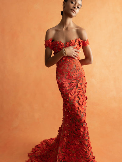 The model is wearing an off the shoulder orange embroidered dress. 
