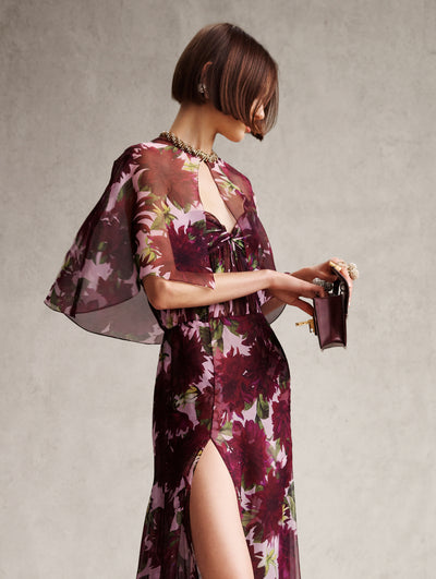 The model is wearing a strapless pink dress with maroon flowers and a matching cape. 