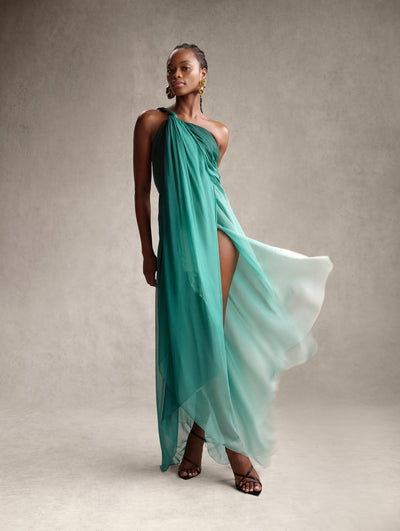 The model is wearing a one-shoulder green ombre dress with a high slit. 