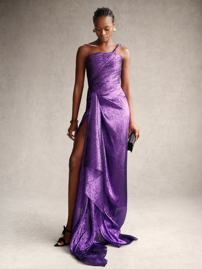 The model is wearing a purple metallic Grecian styled-dress with a slit and shoulder strap. 