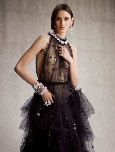 The model is wearing a black tulle halter-neck dress with black ruffles on the skirt and black sequin applique. 