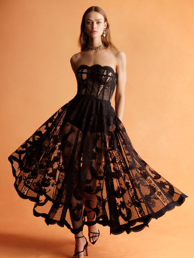 The model is wearing a strapless black lace midi dress. 