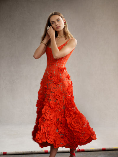 The model is wearing a sleeveless red dress with large taffeta roses embroidered on the skirt. 
