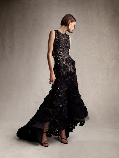 The model is wearing a black high neck sequin evening gown with taffeta black roses. 