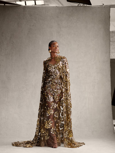The model is wearing a strapless evening gown with gold sequin roses embroidered throughout and the matching cape. 