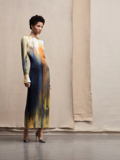 The model wears a long sleeve abstract brushstrokes dress in tones of blue, orange and yellow. Side view