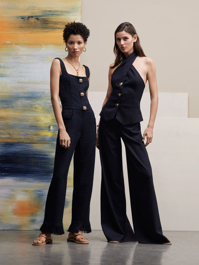 Two models pose together. The model in the left wears a navy tweed set, and the model in the right wears a navy pin stripe set with a halter top.