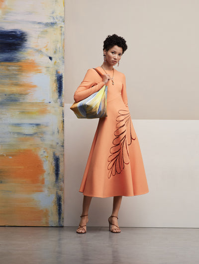 The model wears a long sleeve peach dress with a leave cutout in the skirt.