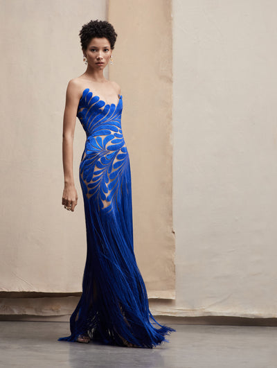 The model wears a royal blue strapless gown, with leave motifs fading into fringe in the bottom.