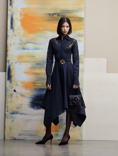 The model poses in a long-sleeve navy collar dress, with an asymmetrical skirt paired with the TRO bag in navy. Front view
