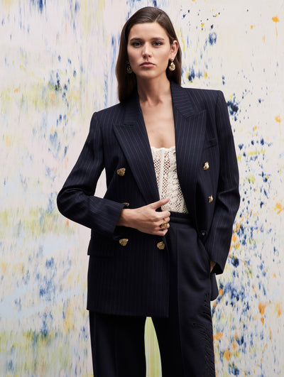 The model poses in a navy pinstripe blazer, with a white crochet corset under, paired with navy pants.