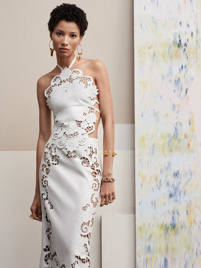 The model poses in a white set with a skirt and halter top, both with cutout details. Front view
