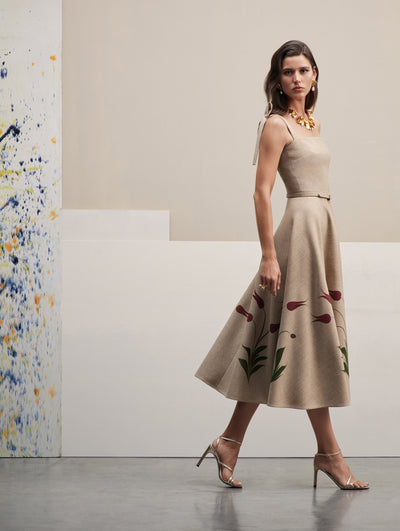 The model wears a beige sleeveless midi dress with floral motifs in the skirt.