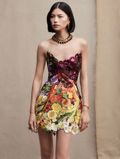 The model wears a strapless mini dress with embroidered flowers in purple, orange, and yellow.