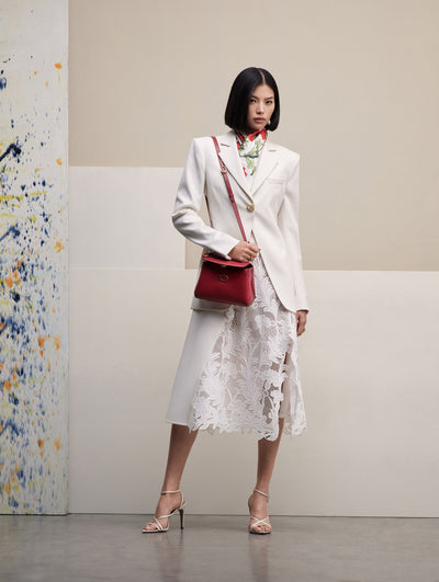 The model poses in a white blazer with a white lace dress under, paired with a white scarf with red flowers and the poppy handbag in red. Front View