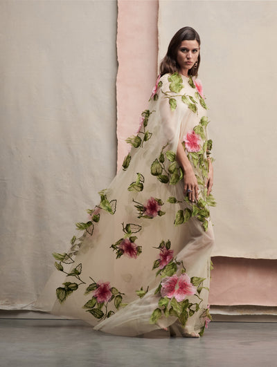 The model poses in a white tulle caftan with pink embroidered flowers.
