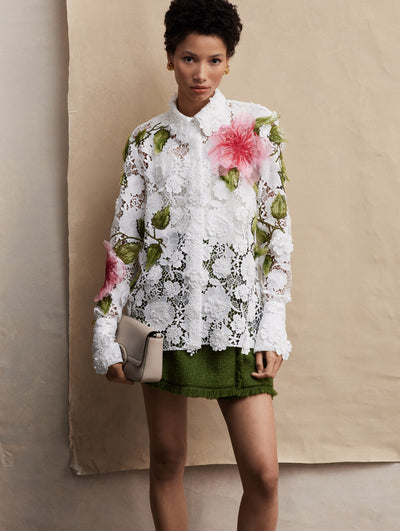 The model poses in a tweed green mini skirt, with a white lace embroidered collar shirt with two pink flowers embroidered.