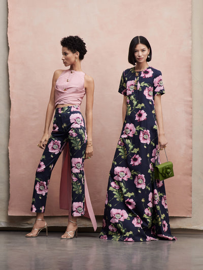 Two models pose together; the model in the left wears navy pants with pink poppies printed across paired with a pink top. The model in the right wears a Shortsleeve maxi dress in the same poppy print.