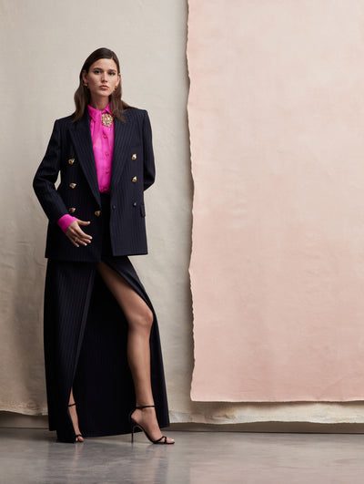 The model wears a navy pinstripe blazer, with a pink button-down blouse under and a matching pinstripe skirt.
