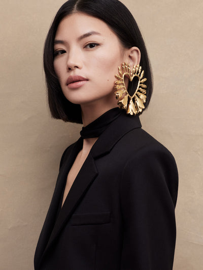 Close up of the model in a black blazer, with large gold heart earrings.