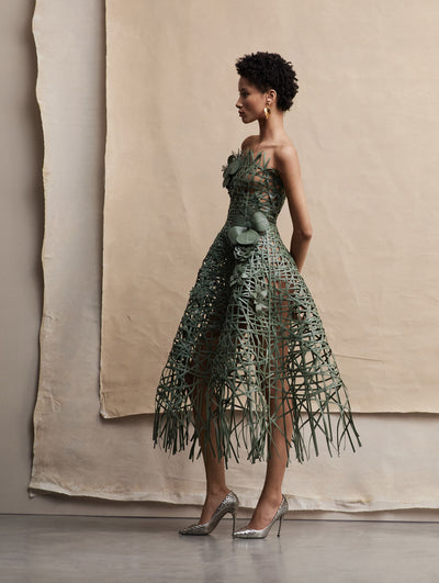 The model poses in a green woven strapless dress with three-dimensional flowers across.