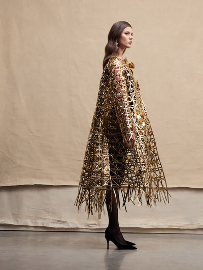 The model poses sideways in a gold woven coat.