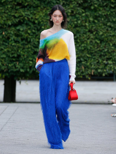 The model is wearing a one shoulder, abstract multicolor knit sweater with lapis fringed fil coupé fabric pants.