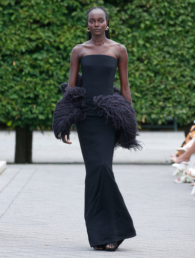 The model is wearing a black strapless evening gown with a feather trim. 