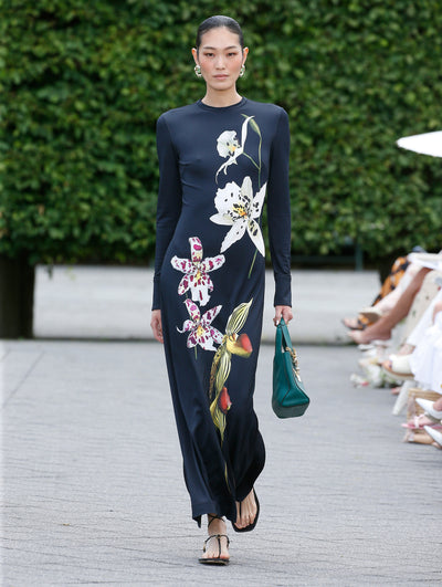 The model is wearing a black, long sleeve, fitted jersey dress with large scale slipper orchids. 