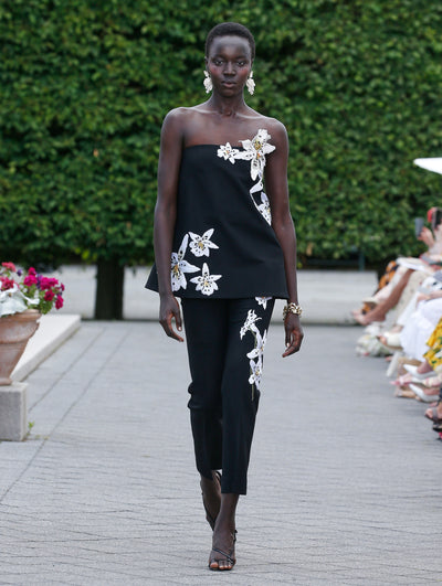 The model is wearing a black strapless blouse with orchid applique and matching black cigarette pants with orchid detailing. 