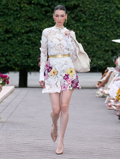 The model is wearing a white floral knit and lace long sleeve top and matching shorts with yellow, pink and purple flower applique. 