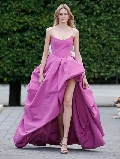 The model is wearing a pink faille strapless gown with a high-low hem. 