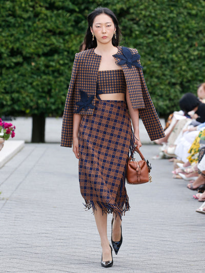A model is wearing a coordinated outfit consisting of a matching cropped, sleeveless top and jacket and a knee-length skirt with a navy and tan geometric pattern.
