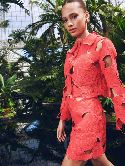 A model poses in a green house in an Oscar de la Renta red laser-cut floral jacket and skirt set. 