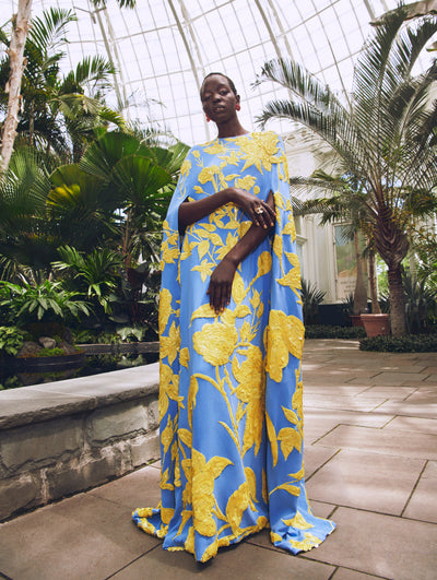 A model poses in a green house in an Oscar de la Renta floral embroidered yellow and blue caftan. 