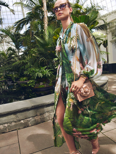 A model poses in a green house in an Oscar de la Renta floral maxi dressed styled with a pave crystal handbag. 