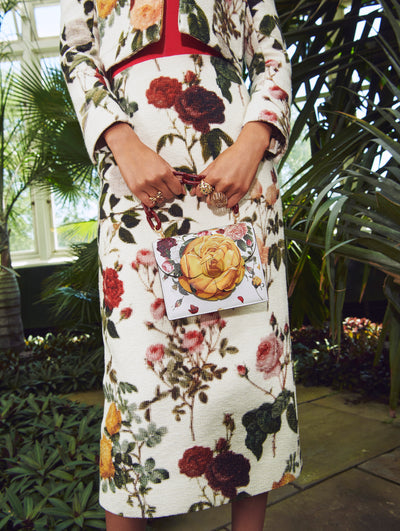 A model poses in a green house in an Oscar de la Renta floral jacket and skirt paired with a matching handbag. 