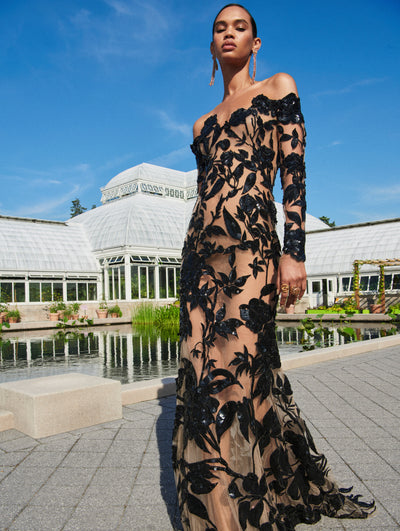 A model poses outside in an Oscar de la Renta black embroidered off-the-shoulder gown. 