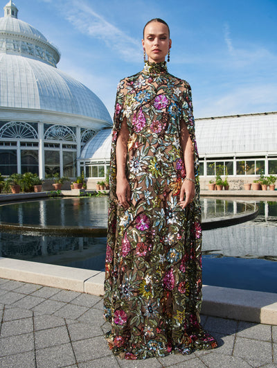 A model wears an Oscar de la Renta sequin embroidered caftan outside in front of a body of water. 