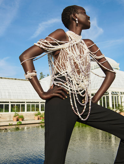 A model poses outside in an Oscar de la Renta pearl embroidered blouse with black trousers. 