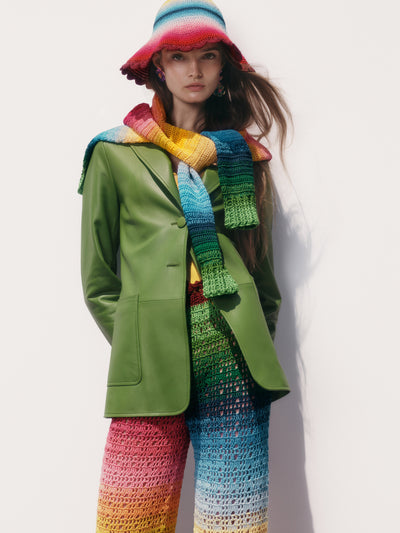 The model is wearing matching rainbow knit crochet pants, sweater and hat with a green leather blazer. 