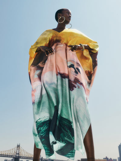 The model is wearing a silk caftan, with hues of orange, peridot and powder blue. 